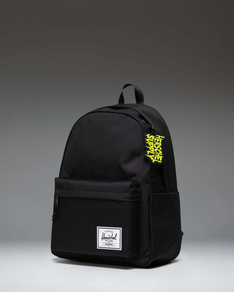 Black Herschel Supply Co. Slime Bag Charm hanging from a backpack zipper.