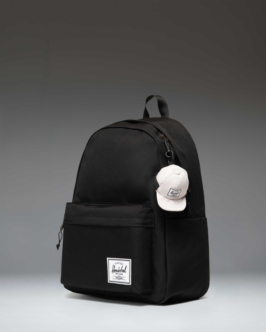 Herschel Supply Co. Sylas Classic Cap Bag Charm in Moonbeam beige, featuring a miniature baseball cap design with an attached metal clip.