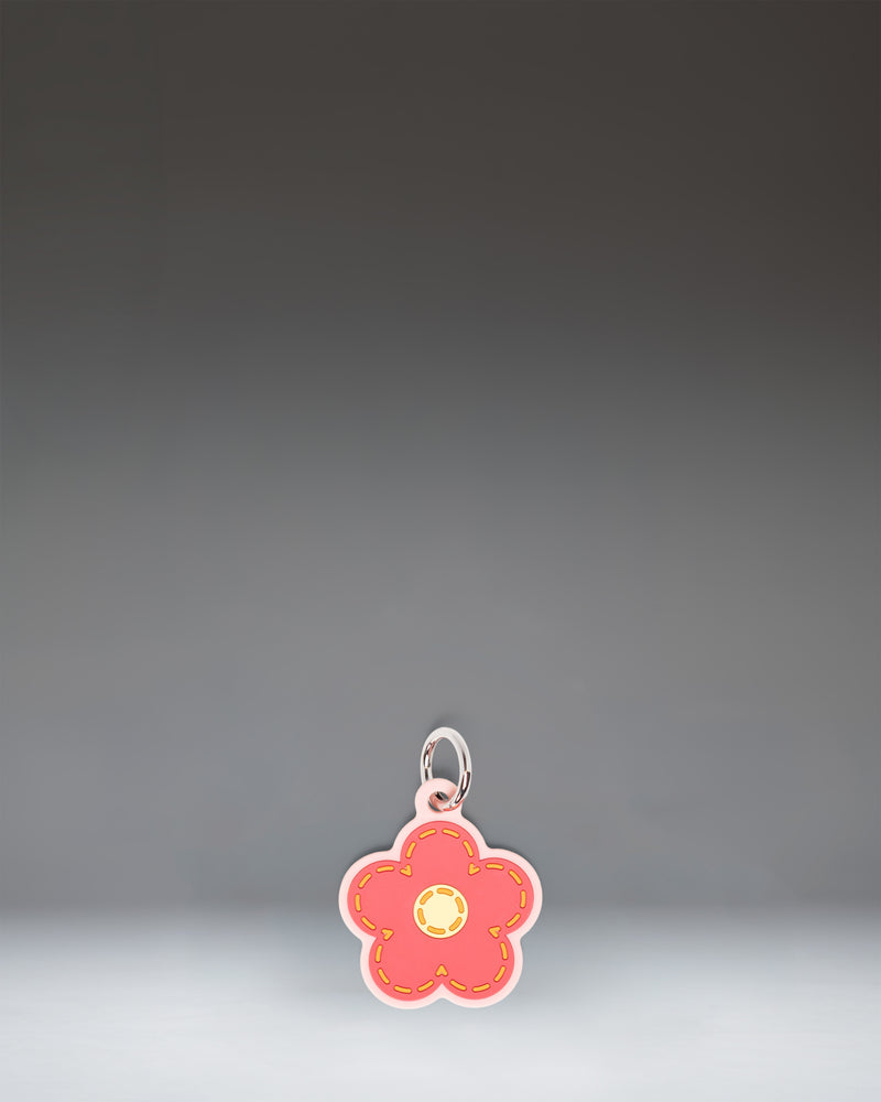 Herschel Daisy Bag Charm in Pink Daisy, featuring a stylized pink daisy flower design with a central yellow disc and attached metal hardware.