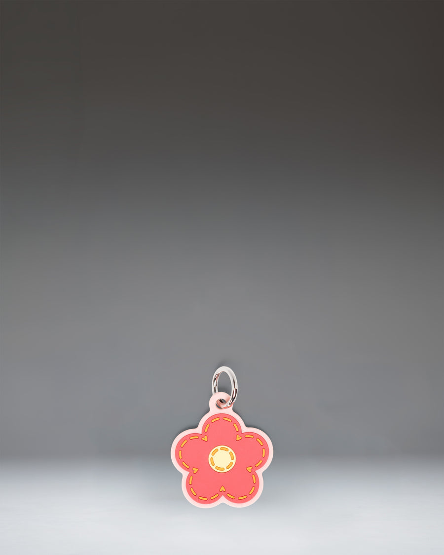 Herschel Daisy Bag Charm in Pink Daisy, featuring a stylized pink daisy flower design with a central yellow disc and attached metal hardware.