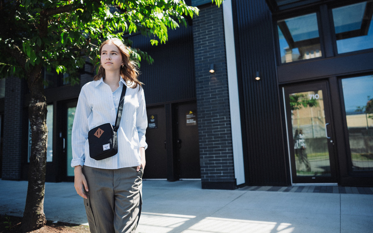 Herschel Supply Co. Heritage Crossbody bag in solid black, showing its compact design, signature diamond detail, and adjustable strap.