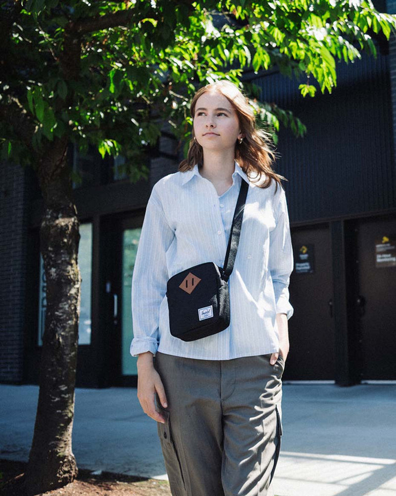 Herschel Heritage Crossbody bag in black featuring a boxy design, signature front diamond patch, zippered closure, and adjustable shoulder strap.