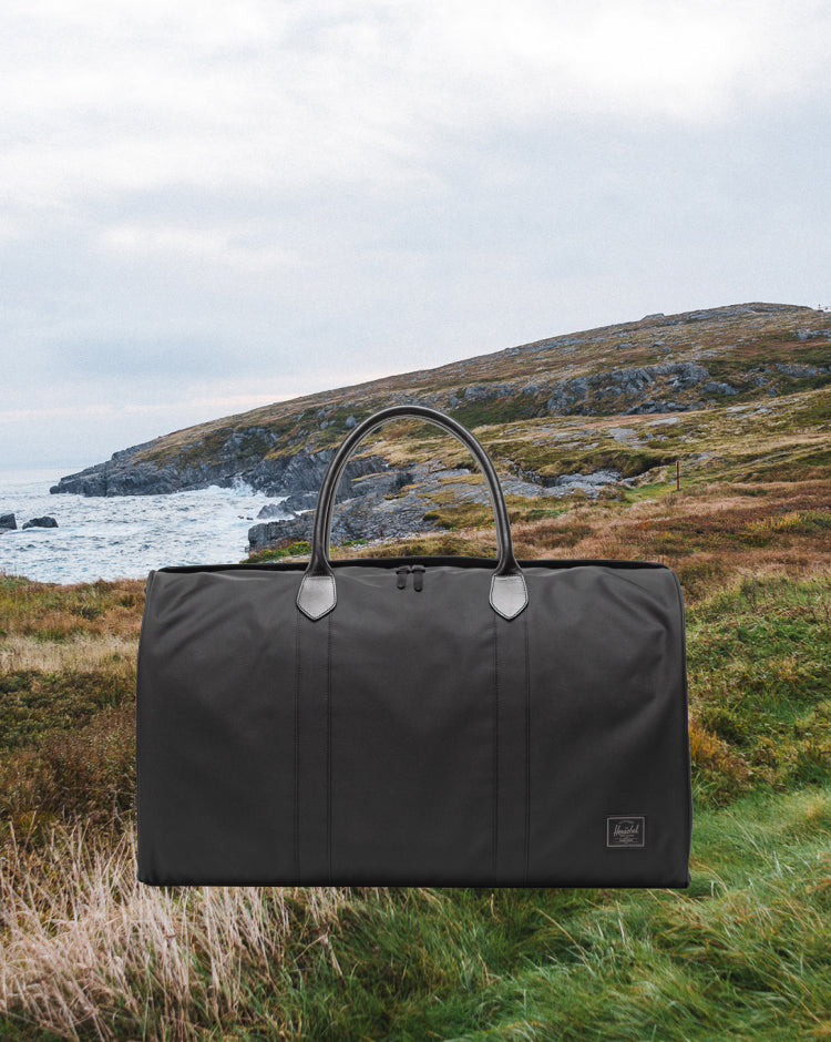 Herschel Supply Co. Novel Duffle bag in black, featuring top handles and a removable shoulder strap, ideal for travel and weekend trips.