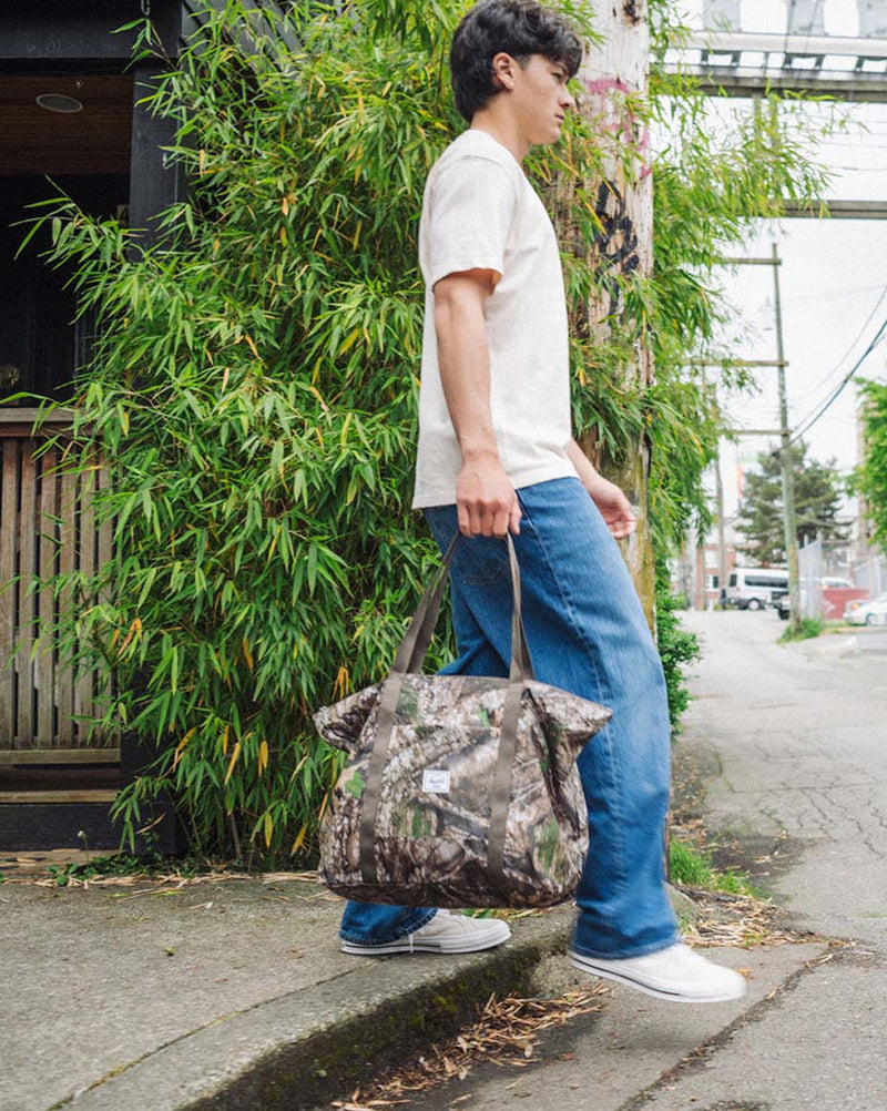 Herschel Supply Co. Realtree Portland Packable Tote bag in the distinctive Realtree APX Camo pattern, showing the lightweight, packable design.