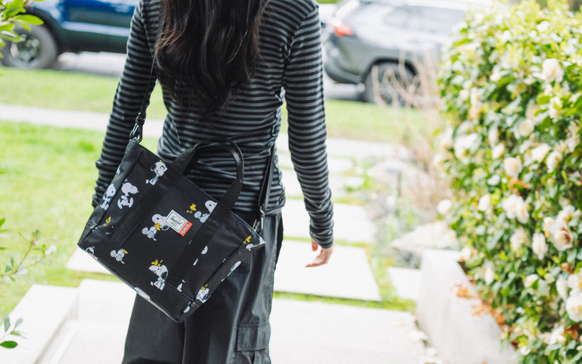 Herschel Supply Co Peanuts Herschel Heritage Small Tote in Snoopy and Woodstock Black on a lifestyle model.