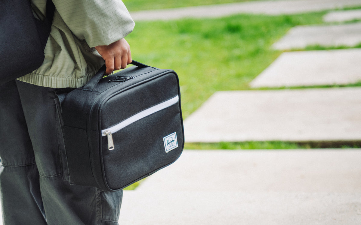 Herschel Supply Co. Pop Quiz Lunch Box in solid black, featuring a front storage zippered pocket and a convenient top carrying handle.