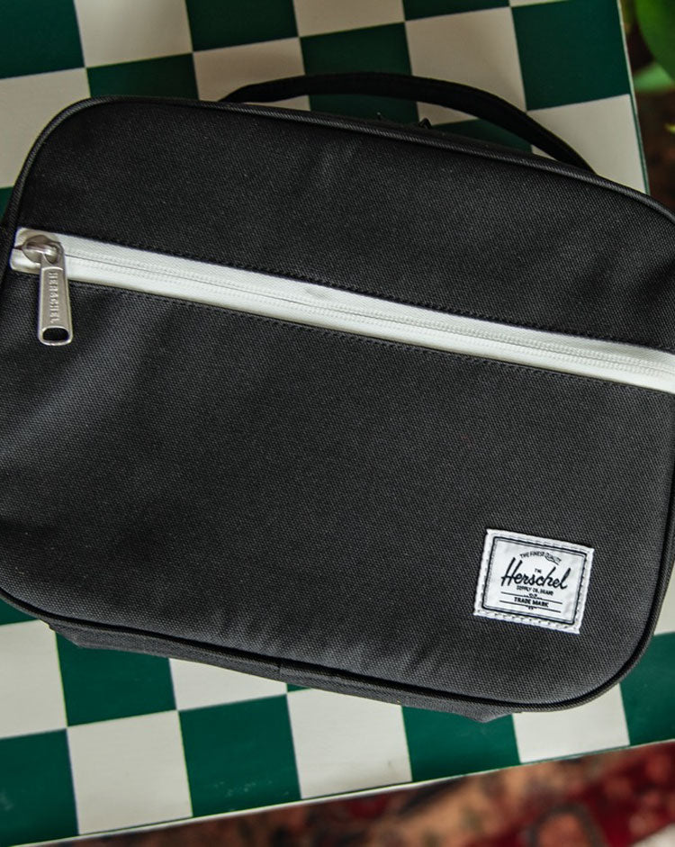 Herschel Supply Co. Pop Quiz Lunch Box Little Herschel in solid black, featuring a front storage pocket and a top carrying handle.