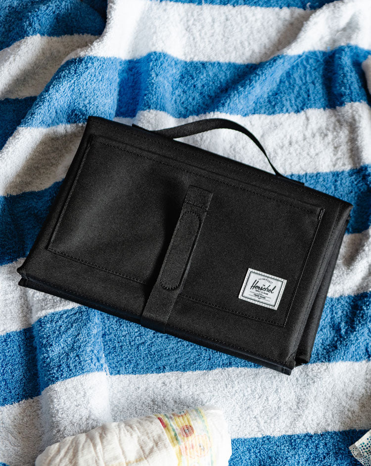 Black Herschel Sprout Change Mat shown folded with its carrying handle and stroller strap attachments.