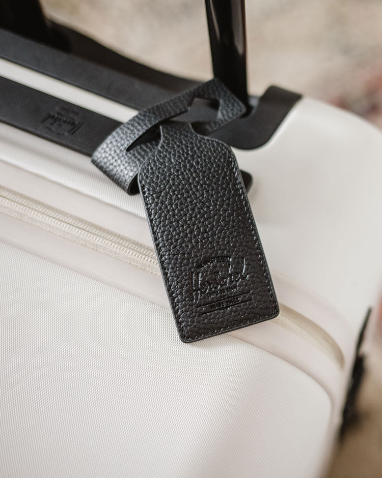 Black vegan leather luggage tag by Herschel Supply Co. featuring a minimalist design with a durable strap and buckle closure.