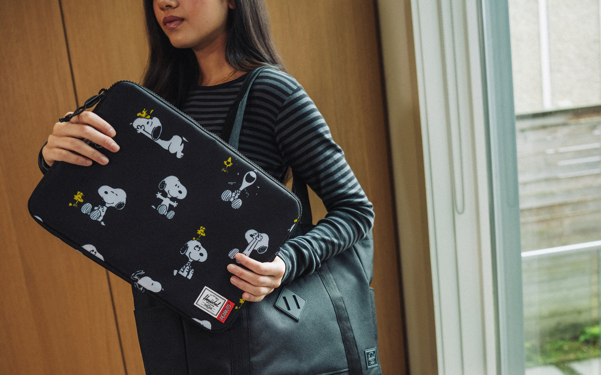 Herschel Supply Co. Peanuts Anchor 14 Inch Sleeve in Snoopy and Woodstock Black featuring a repeating pattern of the classic characters.