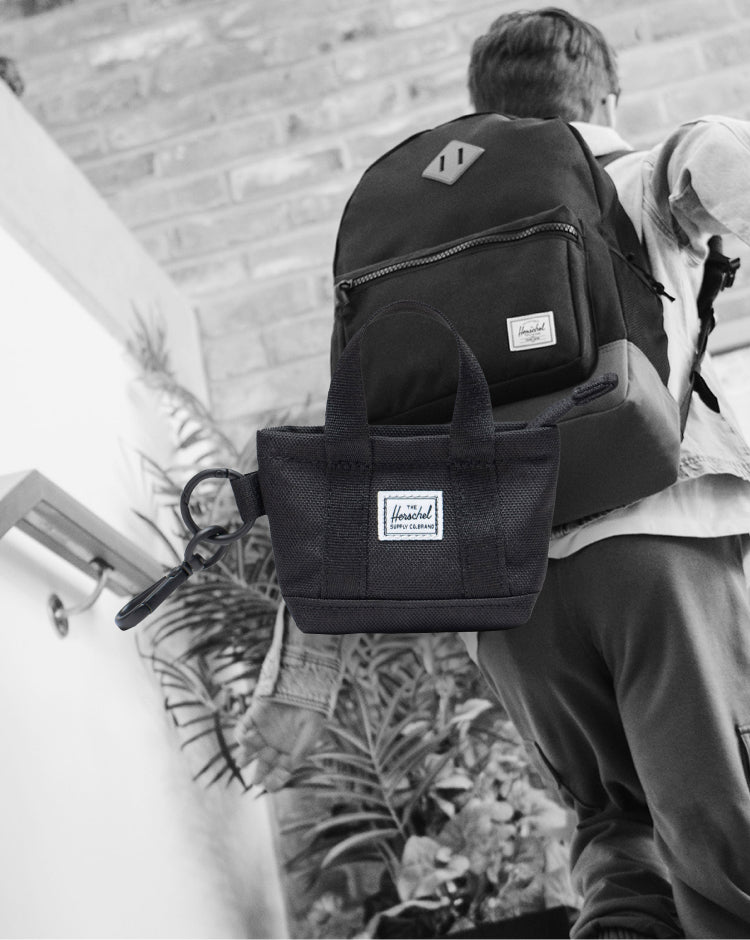 Herschel Supply Co. Heritage Tote Bag Charm in black, showing the miniature backpack design with a zipper pocket and a clip.